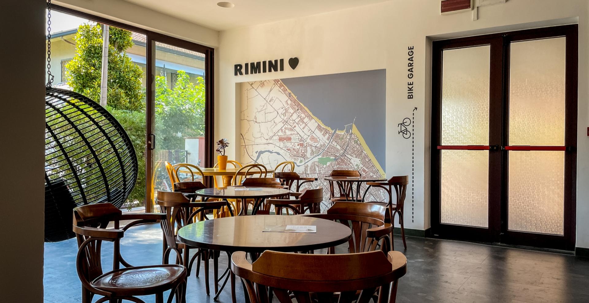 Sala luminosa con mappa di Rimini, sedie in legno e altalena sospesa.