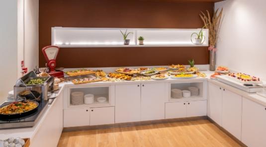 Buffet con varietà di piatti, decorazioni semplici e ambiente luminoso e accogliente.