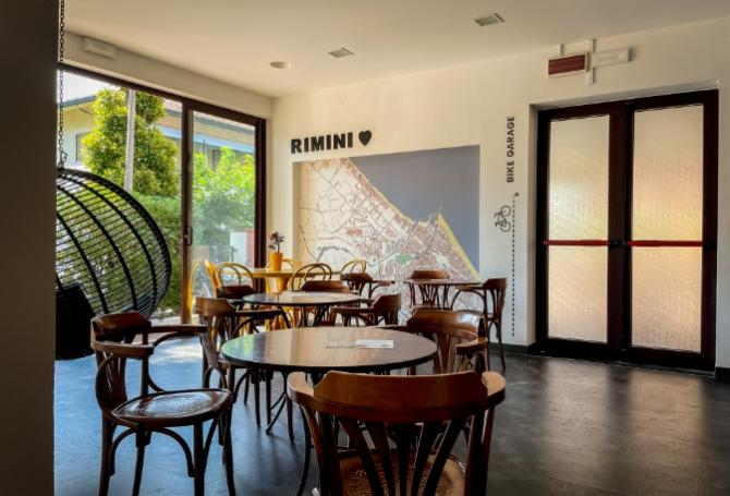 Sala con tavoli e mappa di Rimini, atmosfera accogliente e luminosa.