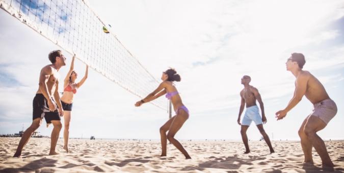 Gruppo di amici gioca a beach volley sulla spiaggia in una giornata soleggiata.