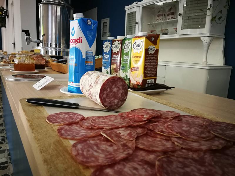 Colazione con salame, latte e bevande vegetali su un tavolo imbandito.