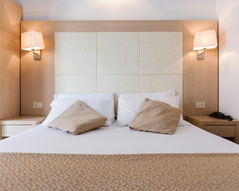 Camera moderna con letto matrimoniale, lampade da parete e cuscini decorativi beige.